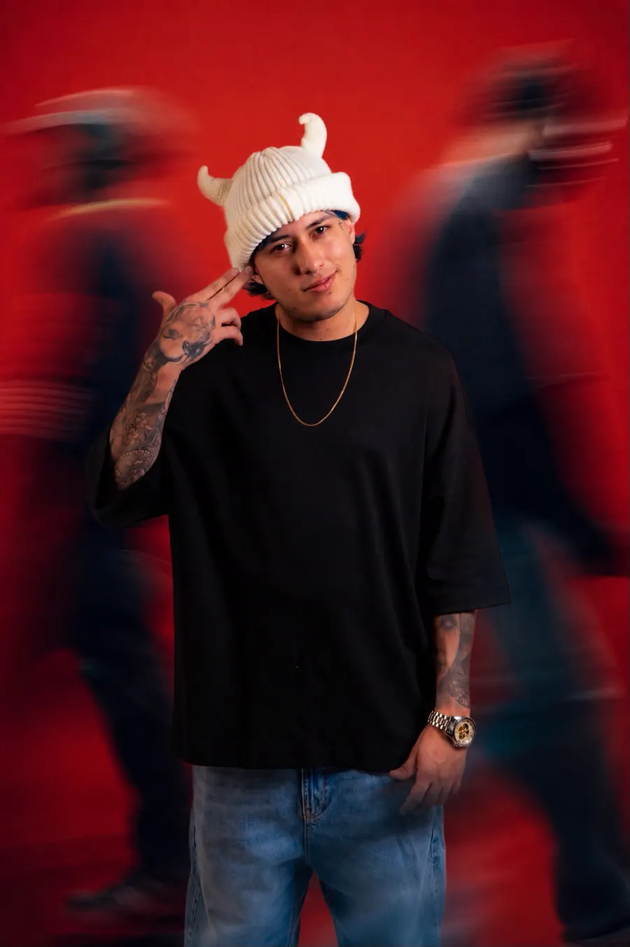 SEVEN77 de pie sobre un fondo rojo, con gorro blanco de cuernos y camiseta negra, entre siluetas de gente en movimiento